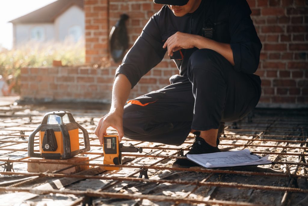 Sitting and using leveling tool. Builder is working on construction site, unfinished building.